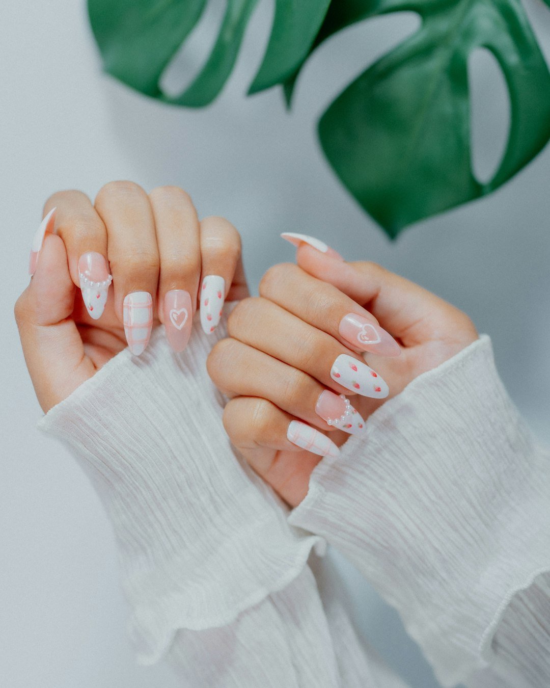 Close-up of pastel pink and white nail art with heart and polka dot patterns, combining playful and elegant design elements.